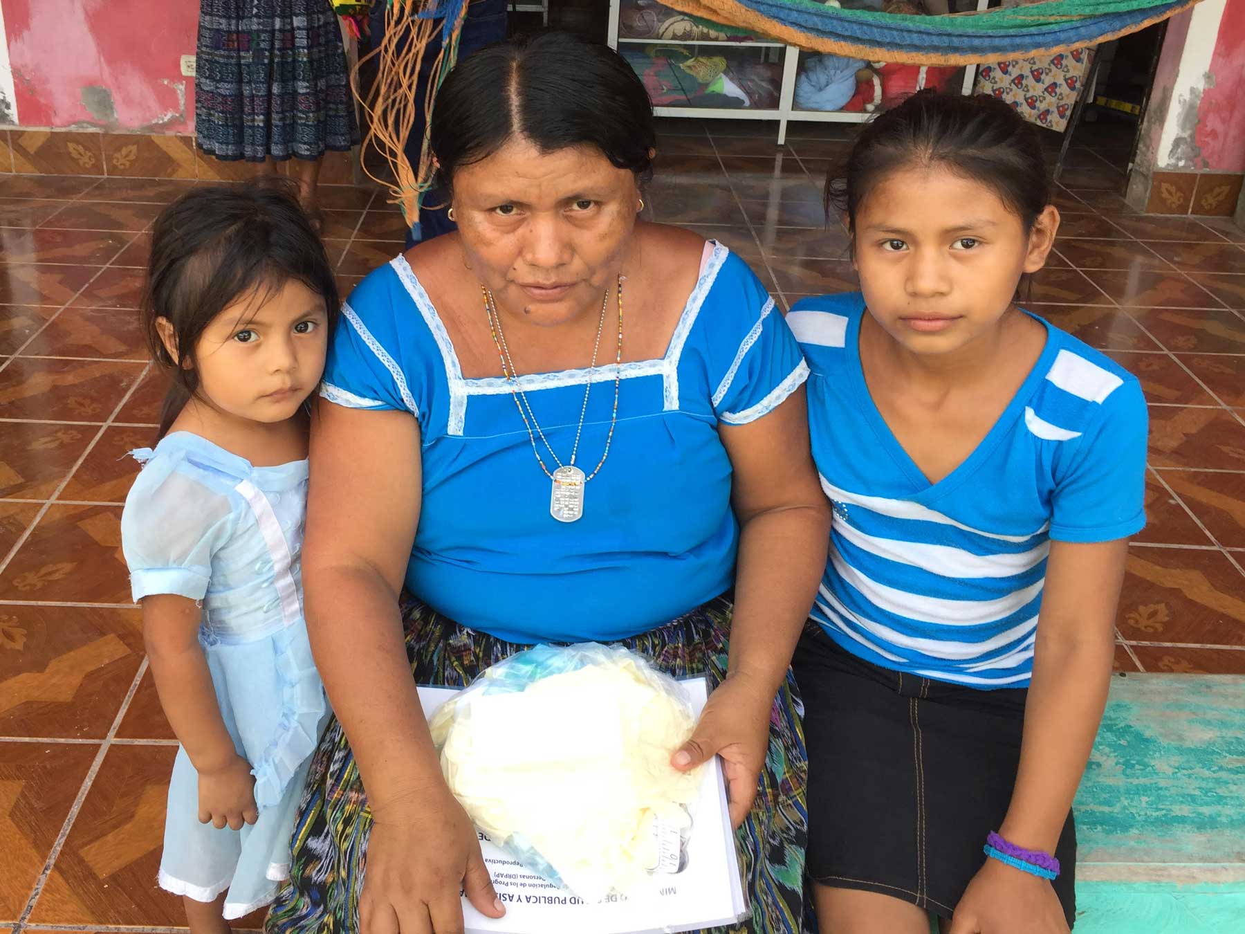 A midwife with two young children, all wearing the colors of the Guatemalan flag