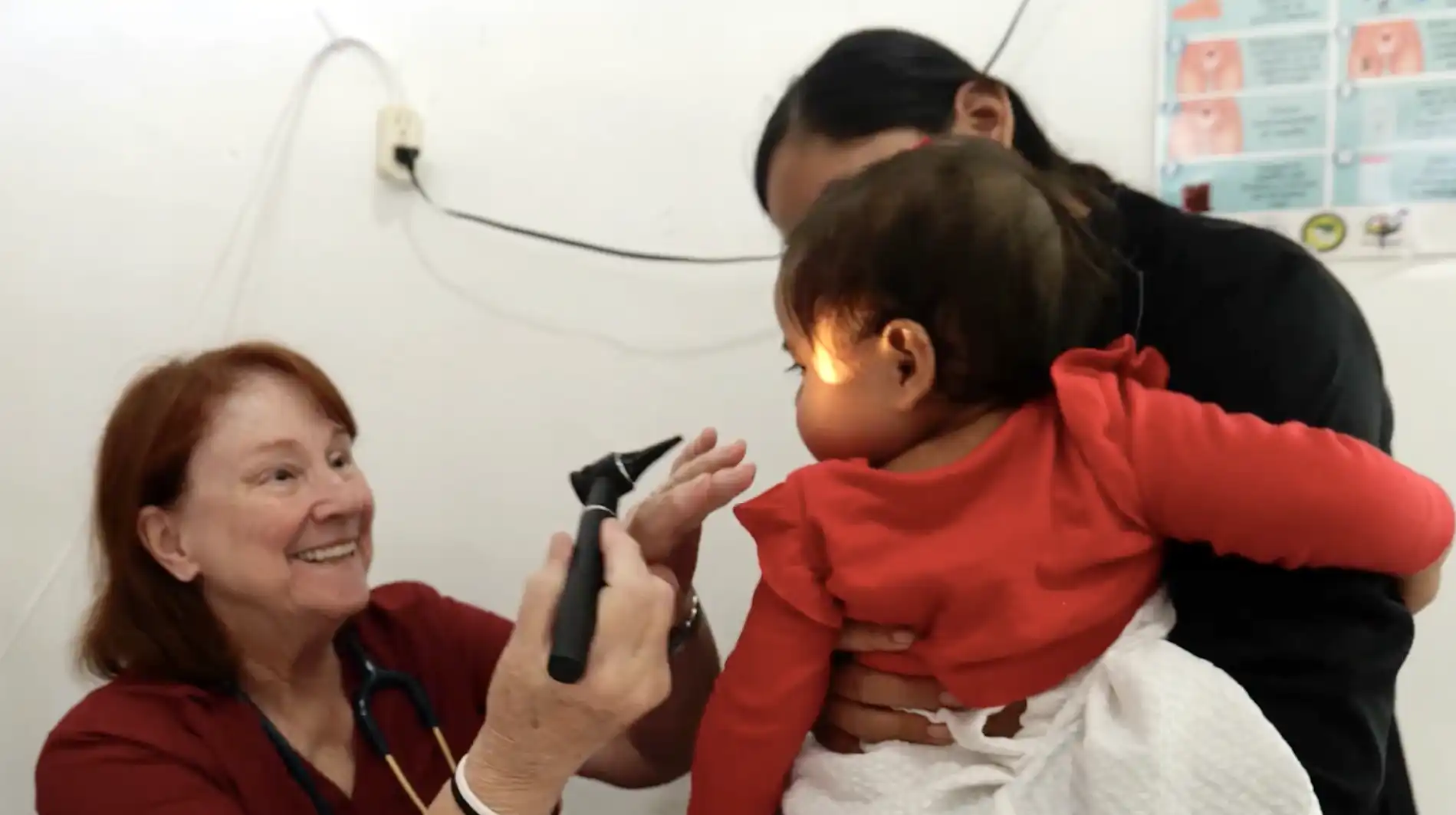 A smiling volunteer examines the eyes of a baby in her mother's arms